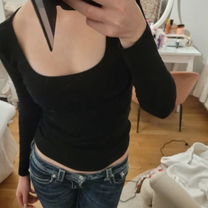 Svart långärmad topp - Säljer en stilren svart långärmad topp med en djup rundad halsringning. Perfekt för en elegant och enkel look. Passar bra till jeans eller kjol. Säljer en lika dan i vit