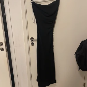 Svart långklänning från Zara - Elegant svart långklänning från Zara med smala axelband och en stilren design. Klänningen har en slits på sidan som ger en extra touch, även knappar vid sidan. Hör av dig för om ni vill ha fler bilder / bilder när den sitter på någon. Otroligt snygg och oanvänd. 