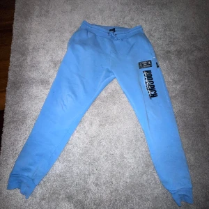 Hoodrich byxor  - Baby blue  mjukisbyxor från Hoodrich med tryck på benet. Byxorna har en avslappnad passform och är perfekta för en chill dag. De har elastisk midja och muddar vid bensluten för extra komfort.