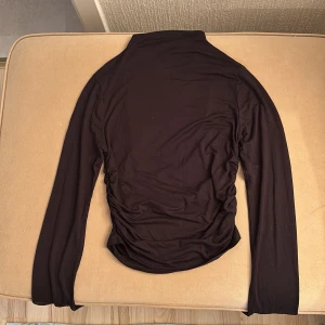 Svart långärmad topp med hög krage - Snygg svart topp med hög krage och långa ärmar och rynkade detaljer på sidorna. Mycket bra skick, knappt använd.