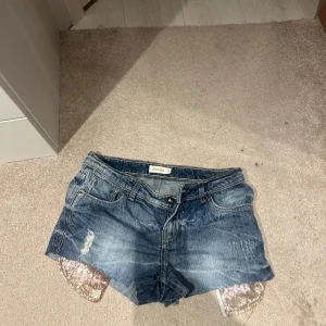 Blå jeansshorts med paljettdetaljer - Snygga blå jeansshorts från Zara med glittriga paljettdetaljer på sidorna. Perfekta för en somrig look med en touch av glamour. De har en klassisk femficksdesign och en knappgylf.