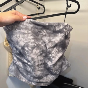 Grå batikmönstrad tubtopp - Säljer en cool grå batikmönstrad tubtopp med dragkedja i sidan. Perfekt för en avslappnad stil med en twist. Passar bra till jeans eller kjol för en trendig look.
