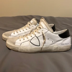 Vita sneakers från Philippe Model - Snygga vita sneakers från Philippe Model med svarta detaljer och snörning. Skorna har en klassisk design med en modern touch, perfekt för en stilren look. Storleken är 46 och sulan i botten har bytts ut från originalet hos en skomakare. Alltså är den mycket mer hållbar än den originella man får från P.M. 