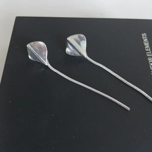 Silverörhängen med lång kedja - Eleganta silverörhängen med en lång, smal kedja som ger en stilren look. Perfekta för att addera en touch av elegans till din outfit. Örhängena har en unik design med en böjd form vid fästet. Aldrig använda.