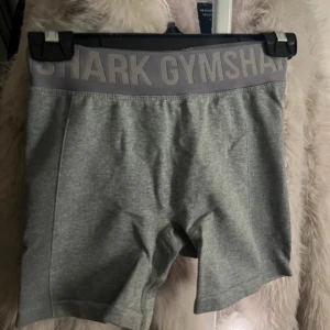 Grå shorts från Gymshark - Säljer ett par grå shorts från Gymshark med bred resår i midjan och logga. Perfekta för träning med en bekväm passform. Materialet är stretchigt och andas bra.