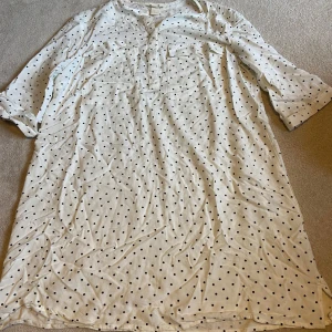 Vit prickig klänning från H&M - Säljer en söt vit klänning med svarta prickar från H&M. Klänningen har trekvartsärmar och en avslappnad passform. Perfekt för en avslappnad dag ute eller en dag på stranden 💞