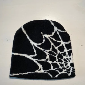 Svart mössa med spindelnätsmönster - Cool svart mössa med ett vitt spindelnätsmönster. Perfekt för att ge en edgy touch till din outfit. Passar bra för kyligare dagar.