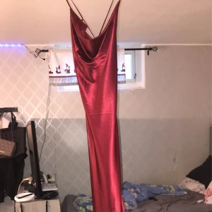 Röd axelbandslös långklänning - Snygg röd långklänning i satin med tunna axelband och en elegant drapering. Perfekt för en festlig kväll med sin glänsande finish och figurnära passform. Det är en Knut också på axelbandet men det är bara på ena använt den två gånger.