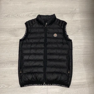 Moncler väst  - Snygg svart dunväst med dragkedja och logotyp på bröstet. Man får även med en svart burberry bälte på köpet. 
