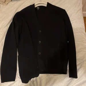 Svart kofta från Uniqlo - Säljer en stilren svart kofta från Uniqlo. Koftan har långa ärmar och knappar framtill, perfekt för en minimalistisk look. Tillverkad i Vietnam.