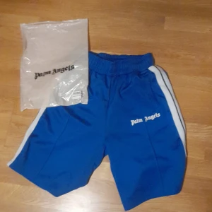 Palm Angels shorts - Säljer ett par blå shorts från Palm Angels med vita ränder längs sidorna. Har bara använt de 2 gånger