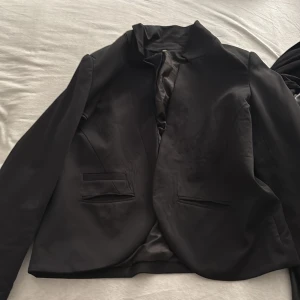 Svart kavaj - Elegant svart kavaj med långärmad design och stilrena linjer. Perfekt för en formell look eller att klä upp vardagsstilen. Kavajen har en klassisk passform och diskreta fickor framtill.