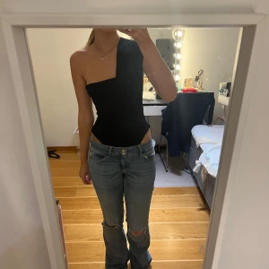 Svart oneshoulder topp - Snygg svart oneshoulder topp som passar perfekt för en stilren look. Toppen har en tight passform och är tillverkad i ett mjukt material som sitter bekvämt mot kroppen.