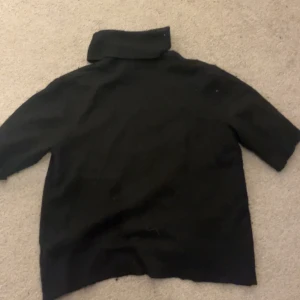 Svart polotröja - Säljer en stilren svart stickad polotröja med trekvartsärm. Perfekt för kyligare dagar och kan enkelt matchas med olika outfits. Tröjan har en klassisk design med en hög krage.