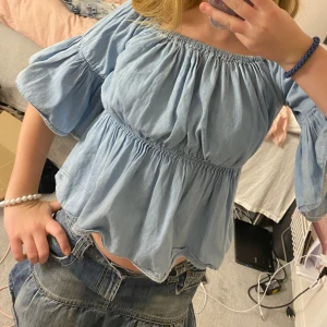 Ljusblå offshoulder blus - Charmig ljusblå offshoulder blus med volangdetaljer. Blusen har en luftig passform och trekvartsärmar, perfekt för en avslappnad stil. Tillverkad i ett mjukt och bekvämt material.