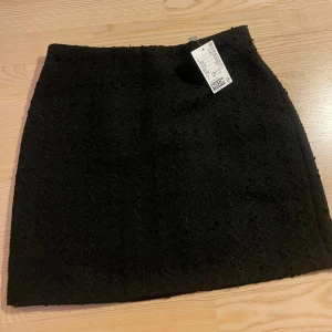 Minikjol - Kort, figurnära kjol i strukturerat material. Kjolen har resår upptill samt dragkedja bak. Är i nyskick med prislapp kvar.