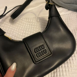 Svart axelväska från Miu Miu - Snygg svart axelväska från Miu Miu i skinn med guld detaljer, tidigare köpt från Plick men inte kommit till användning. Ser helt ny ut.