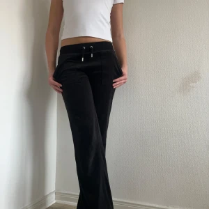 Svarta byxor från Juicy Couture - Snygga svarta byxor från Juicy Couture i en mjuk och bekväm design. Byxorna har en dragsko i midjan och fickor med knappar framtill. Midjan är stretchig. Jag är 169 för referens. 💗