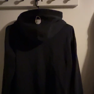 Svart hoodie från Sail Racing - Snygg svart hoodie från Sail Racing med logga på bröstet. Perfekt för en avslappnad stil. Den har en klassisk passform och en bekväm huva.