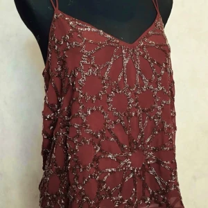 Vinröd linne med paljettdetaljer - Assnyggt vinrött linne med tunna axelband och glittriga paljettdetaljer. Perfekt för en kväll ute eller en festlig tillställning. Linnet har en v-ringad design och en öppen rygg😚