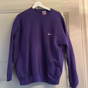 Lila sweatshirt från Nike - Säljer en snygg lila sweatshirt från Nike med klassisk logga på bröstet. Tröjan har långa ärmar och en rund halsringning. Perfekt för en avslappnad stil. Passar bra till både jeans och träningsbyxor.