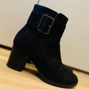 Svarta boots med spänne - Snygga svarta boots i mocka med en bred klack och dekorativt spänne. Perfekta för höst och vinter, med dragkedja på sidan för enkel på- och avtagning.