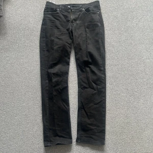 Svarta Levis 514 jeans - Säljer ett par svarta Levis 514 jeans i storlek W30 L32. Klassisk design med fem fickor och dragkedja. Perfekta för en stilren look. Det finns en liten defekt som man ser på bilden och så är de lite solblekta.