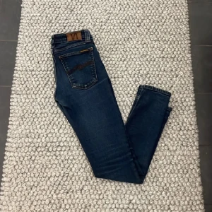Nudie Jeans - Snygga mörkblå jeans från Nudie. De har en slim passform och är tillverkade i ett stretchigt denimtyg för extra komfort. Perfekta för en stilren look.27W-30L passar runt 165cm
