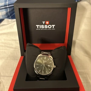 Tissot herrklocka i silver - Elegant herrklocka från Tissot med en stilren grön urtavla och datumvisning. Klockan har ett robust armband i silverfärgat rostfritt stål och kommer i originalförpackning. Perfekt för den som söker en tidlös accessoar. Pris kan diskuteras 