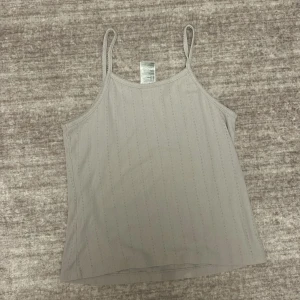 Beige linne från H&M - Säljer ett enkelt och stilrent beige linne från H&M. Linnet har smala axelband och en lätt ribbad struktur. Perfekt för varma dagar eller som lager under andra plagg.