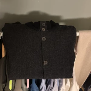 Mörkgrå kappa från Giorgio Armani - Säljer en elegant mörkgrå kappa från Giorgio Armani, tillverkad i Italien. Den har en stilren design med knappar framtill och en hög krage. Perfekt för att hålla stilen under kyligare dagar. Strl:M. Kom med förslag på pris i dm så löser vi något som passar dig!