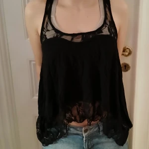 Svart spetslinne - Säljer ett svart linne med spetsdetaljer. Linnet har en lös passform och är ärmlöst med en vacker spetsdesign både fram och bak. Perfekt för en stilren och elegant look.