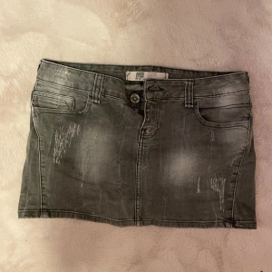 Grå jeanskjol - Snygg grå jeanskjol med slitna detaljer och klassisk femficksdesign. Kjolen har en knapp och dragkedja framtill. Perfekt för en avslappnad stil. Det är en mini kjol som är Lågmidjad kanoter andvänd 