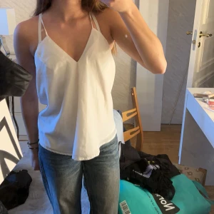 Vit festlig topp - Säljer en stilren vit linnetopp med smala axelband och v-ringning. Köpt secondhand 