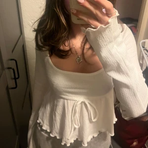 Vit ribbad topp med knytband - Säljer en söt vit ribbad topp med långa ärmar och knytband i midjan. Toppen har en volangdetalj vid nederkanten som ger en fin touch. Nypris 199kr💞