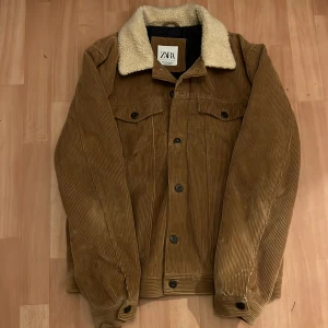 Brun manchesterjacka från Zara - Säljer en snygg brun manchesterjacka från Zara med en mysig fuskpäls-krage. Jackan har knappar framtill och två bröstfickor med knappar. Perfekt för höst, vår  och vinter!