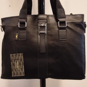 Svart Hand / Axelväska / datorväska  - Snygg svart datorväska med stilrena detaljer. Väskan har en praktisk dragkedja framtill och robusta handtag. Perfekt för att bära med sig datorn med stil. Huvud fack med dragkedja, finns en fack inuti med dragkedja, 2 fickor utan dragkedja.                                                   Mått 37.00*28.00*8,50 cm 