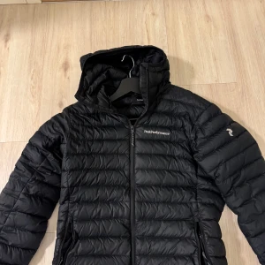 Svart dunjacka från Peak Performance - Säljer en stilren svart dunjacka från Peak Performance. Jackan har en dragkedja framtill och är långärmad med en huva för extra värme. Perfekt för kyliga dagar. Använd fåtal gånger. Tveka inte att höra av er vid intresse.