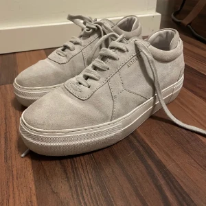 Grå sneakers från Axel Arigato - Snygga grå sneakers i mocka från Axel Arigato med klassisk snörning och en stilren design. Perfekta för en avslappnad och trendig look.