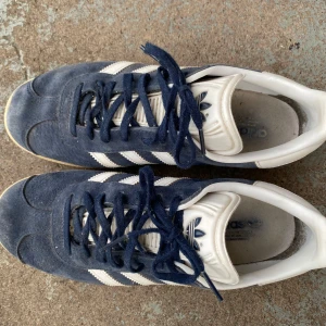Adidas Gazelle stl 38 - Adidas Gazelle skor, mörkblå. Köptes år 2018. Används några gånger. Väldigt dammiga efter att ha stått i skohyllan i flera år. Storlek 38 dam. 