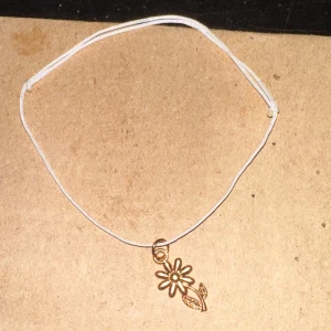 Vitt armband med blomma - Säljer ett enkelt och stilrent vitt armband med en söt blomma i guld. Perfekt för att ge en subtil touch av elegans till din outfit. Armbandet är justerbart och passar de flesta handleder.