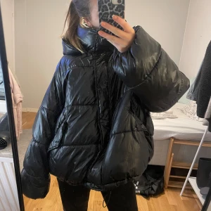 Svart oversized pufferjacka - Säljer denna supermysiga svarta pufferjacka som är perfekt för kalla dagar. Den är oversized och har en hög krage. Jackan har långa ärmar och en dragkedja framtill. Använd 2 säsonger men fortfarande i bra skick.