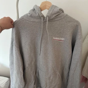 Balenciaga hoodie - En grå hoodie från Balenciaga i unisex modell. Logo på vänster bröst samt stort på ryggen   Inköpt på Mytheresa, kvitto på originalköpet finns att få för att kontrollera äktheten 