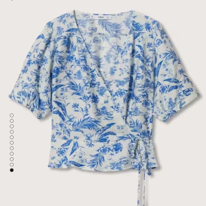 Blommig omlottopp i blått och vitt - Säljer en superfin blommig/mönstrad omlottopp från Mango i blått och vitt. Toppen har korta ärmar med tre små knappar och ett knytband i midjan för en snygg passform. 💕 Aldrig kommit till användning, lite skrynklig då den legat i gaderoben ett tag