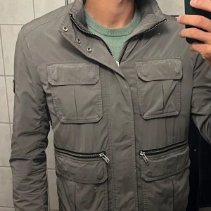 J.Lindeberg jacka / field jacket - Säljer en fet field jacket från J.Lindeberg i en ovanlig silvergrå färg som är svår att hitta! Den är i bra skick, utan defekter och i storleken M. Skulle säga att den passar folk allt mellan 165-185 cm. Nypris ca. 4000