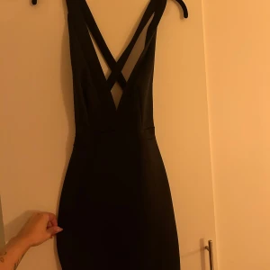 Svart klänning från NLY One - En suuupersnygg klänning från Nelly i storlek S. Djupt V-ringad med korsade band i ryggen och knä-kort. Använd 1 gång. 