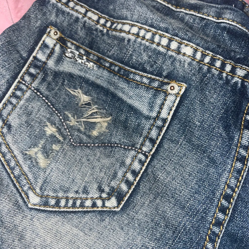 Blåa lågmidjade jeansshorts med döskallar på framsidan och cool design på bakfickorna💕 Storlek 25 Kom privat för frågor!. Shorts.