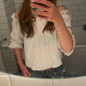 Vit offshoulder blus - Säljer en söt vit offshoulder blus med broderade detaljer och volanger. Perfekt för sommardagar. Passar bra till jeans eller kjol för en avslappnad look.