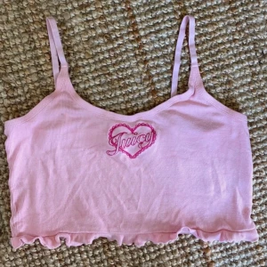 Rosa croppad linnetopp från Juicy Couture - Söt rosa croppad linnetopp från Juicy Couture med justerbara axelband och volangdetaljer i nederkant. Toppen har ett broderat hjärta med texten 'Juicy' på framsidan. Vintage!!