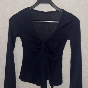 Svart långärmad topp från Gina Tricot - Snygg svart långärmad topp från Gina Tricot i storlek XXS. Toppen har en v-ringad design med knytning framtill, perfekt för en stilren look.